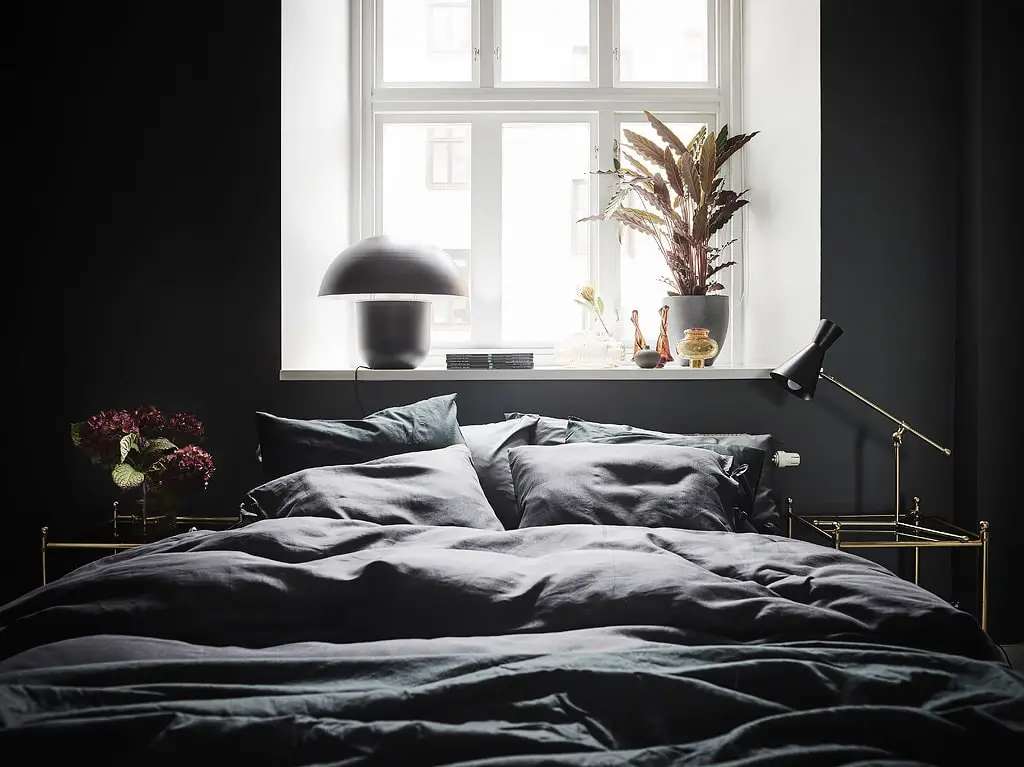 De gouden nachtkastjes zorgen voor een vleugje glamour in deze slaapkamer met zwarte muren.